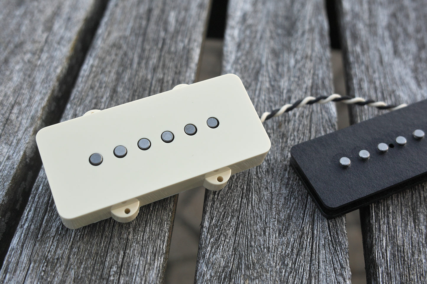Two Lake Surfer model pickups for Jazzmaster-style guitars on a wood background. One has a parchment cover on and the other does not have a cover on.