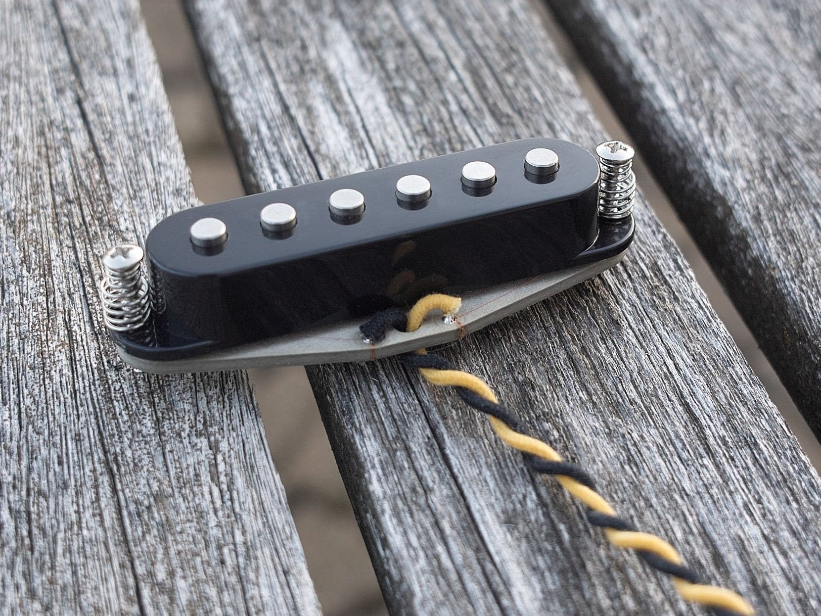 A single guitar pickup for stratocaster guitars with flat poles and a black cover